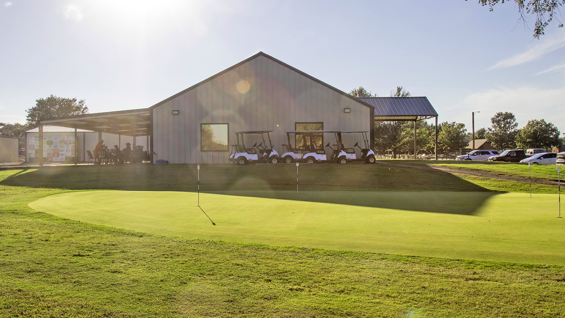 Sayre National Golf Course clubhouse with sun shining in the background and lush green foreground.
